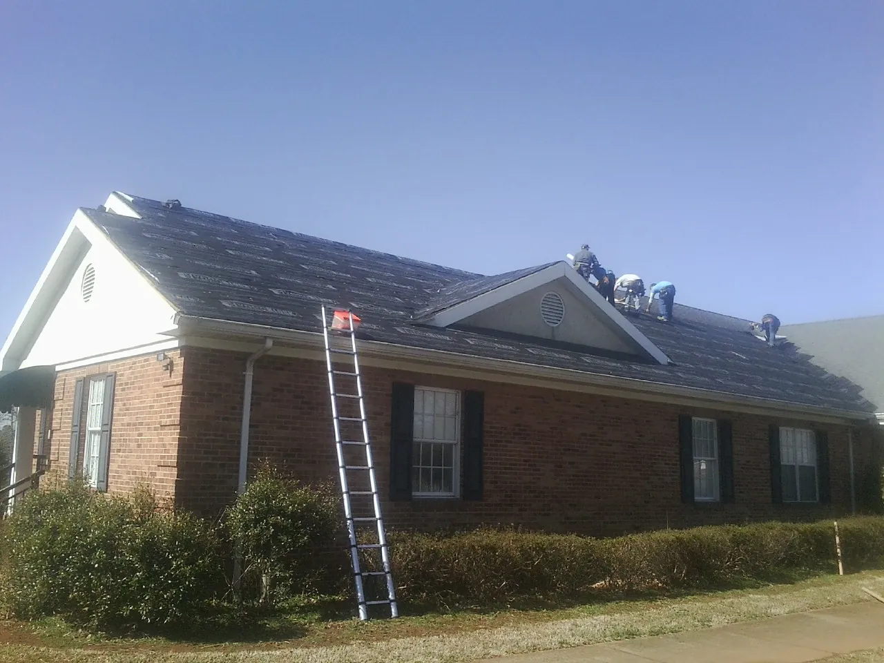 Crew tearing shingles off a brick ranch roof with a ladder set — Metal Roof Repair work by our crew in Buffalo